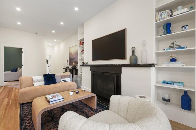 living room featuring a glass covered fireplace, built in shelves, wood finished floors, and recessed lighting