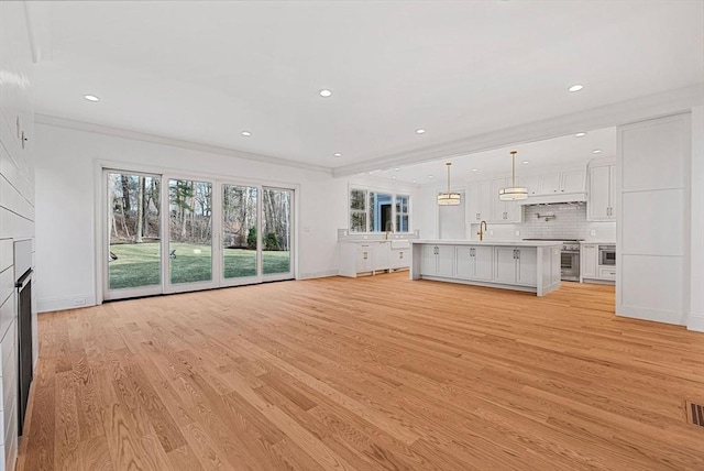 unfurnished living room with recessed lighting, ornamental molding, and light wood finished floors