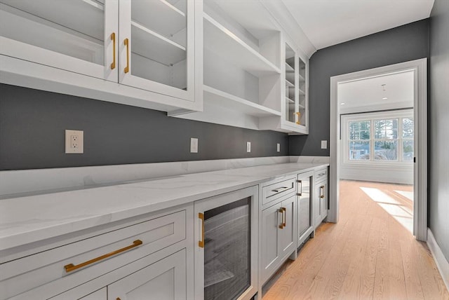 kitchen featuring light stone counters, glass insert cabinets, wine cooler, and light wood-style flooring