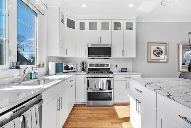 kitchen featuring stainless steel appliances, a sink, light wood-style flooring, and white cabinetry