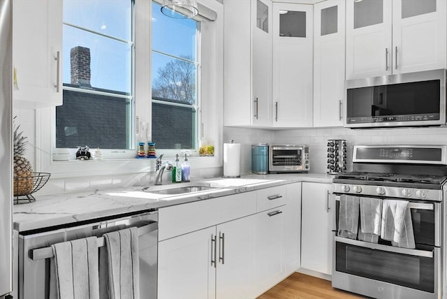 kitchen featuring stainless steel appliances, white cabinetry, a sink, and light stone countertops