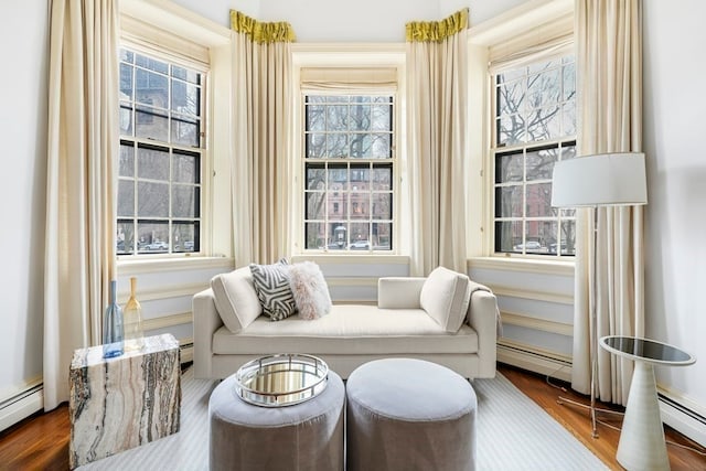 living area with a wealth of natural light, hardwood / wood-style floors, and a baseboard heating unit