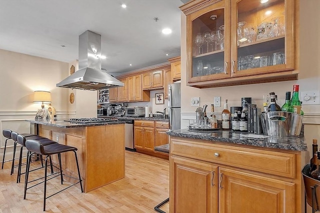 110 O St Unit 1, Boston, MA 02127 - kitchen with island exhaust hood, a kitchen bar, light wood finished floors, and glass insert cabinets