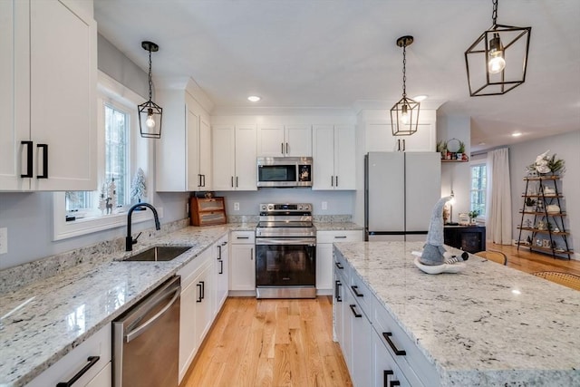 kitchen featuring appliances with stainless steel finishes, sink, pendant lighting, light hardwood / wood-style flooring, and white cabinetry