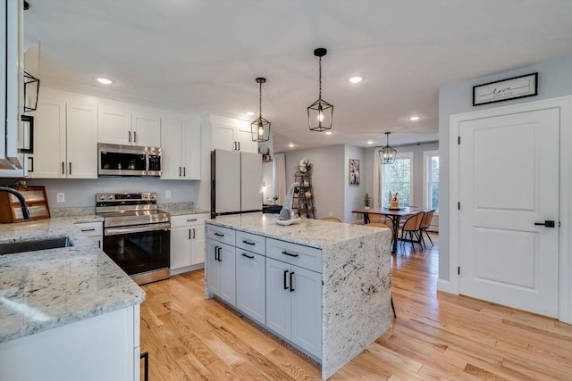 kitchen featuring appliances with stainless steel finishes, light wood-type flooring, light stone counters, a kitchen island, and white cabinetry