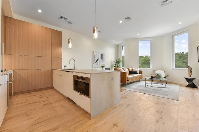 kitchen featuring decorative light fixtures, light brown cabinets, sink, kitchen peninsula, and light hardwood / wood-style flooring