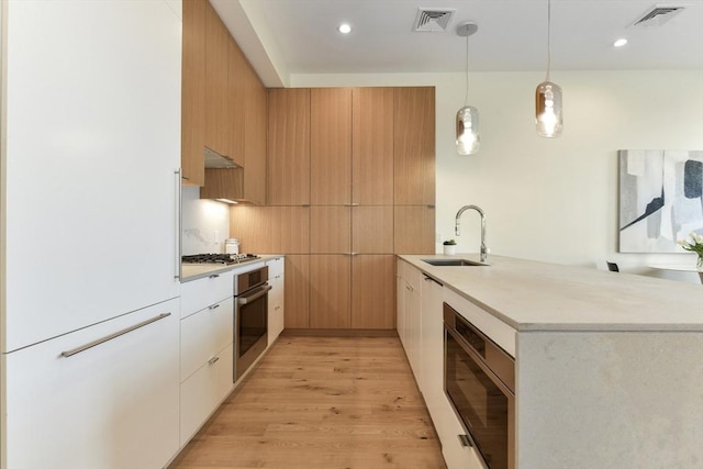 kitchen with built in appliances, light brown cabinetry, hanging light fixtures, sink, and white cabinets