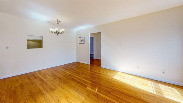 unfurnished room featuring light wood-style flooring, baseboards, and an inviting chandelier