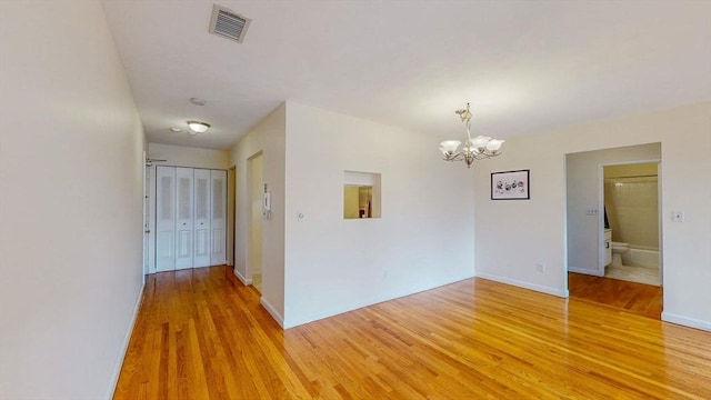 empty room with light wood finished floors, visible vents, baseboards, and a notable chandelier