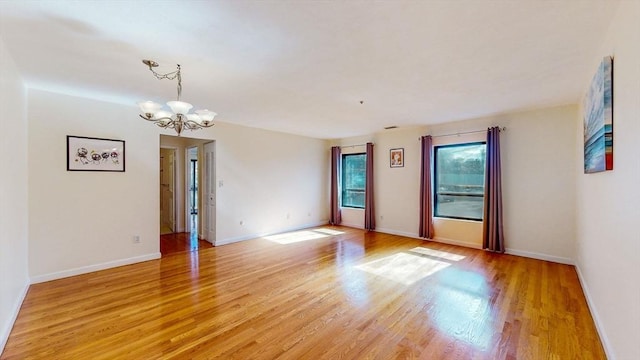 spare room with a notable chandelier, light wood-style flooring, and baseboards