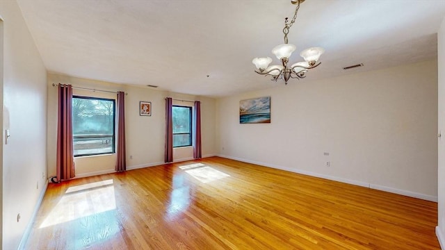 empty room featuring a notable chandelier, baseboards, light wood-style floors, and visible vents