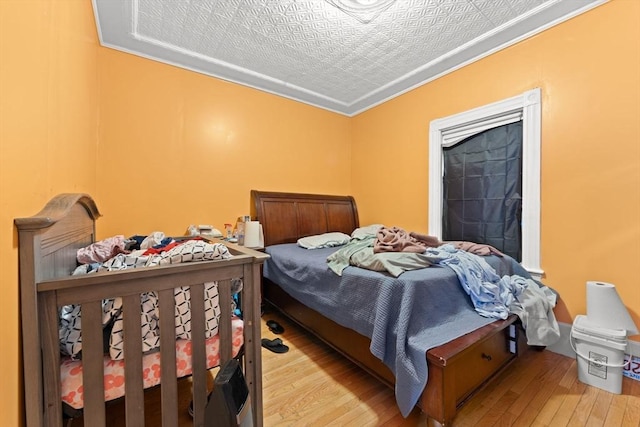 bedroom with a textured ceiling, light hardwood / wood-style floors, and ornamental molding