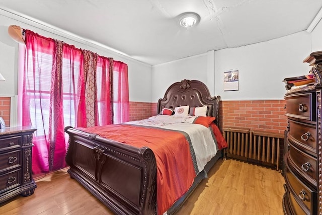 bedroom with radiator heating unit, light hardwood / wood-style flooring, and multiple windows