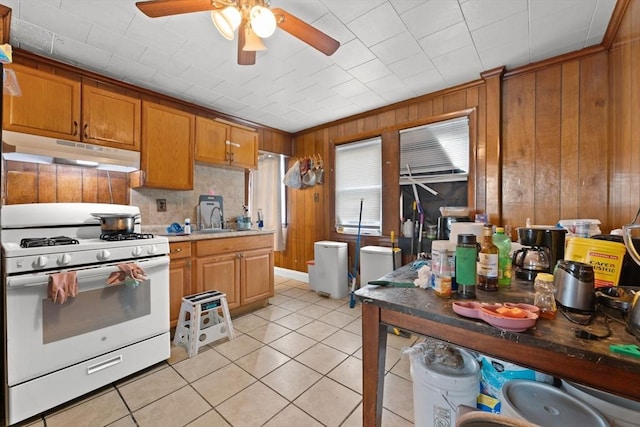 kitchen with sink, wooden walls, ceiling fan, light tile patterned flooring, and white range with gas cooktop