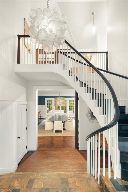 staircase featuring stone finish flooring, a towering ceiling, and a notable chandelier