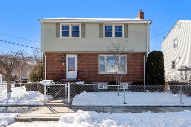 colonial house with a fenced front yard, a chimney, a gate, and brick siding