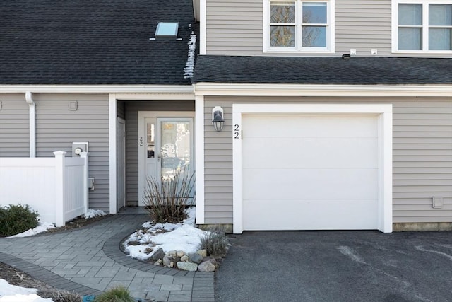 doorway to property featuring an attached garage, driveway, and roof with shingles