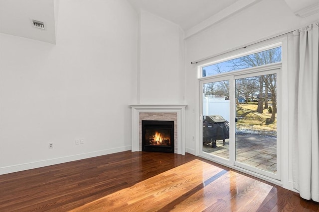 unfurnished living room with visible vents, baseboards, wood finished floors, and a lit fireplace