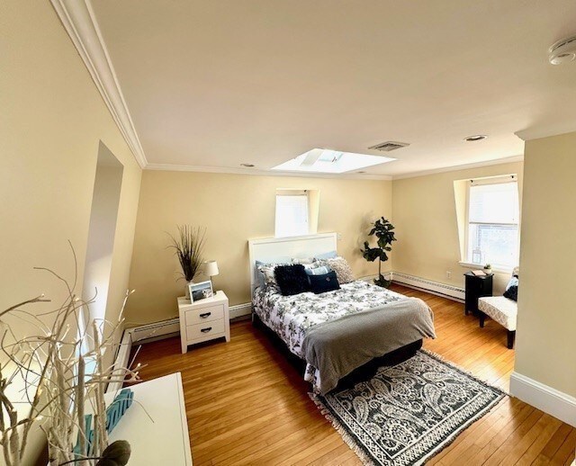 bedroom featuring visible vents, a baseboard heating unit, wood finished floors, crown molding, and baseboards