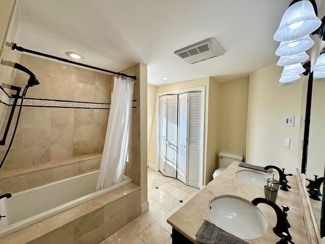 bathroom with tiled shower / bath combo, double vanity, visible vents, and a sink