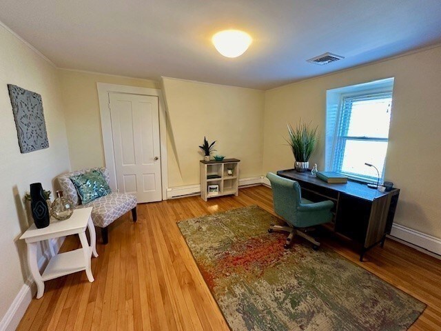 office space featuring visible vents, baseboards, wood finished floors, and a baseboard radiator