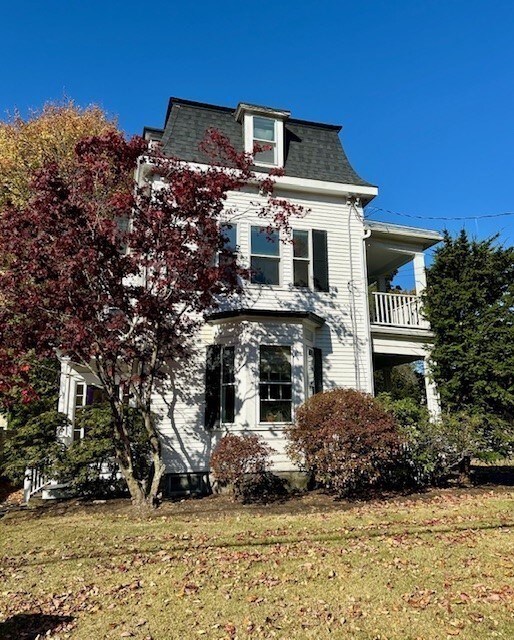 view of front facade with a front lawn, a balcony, and mansard roof