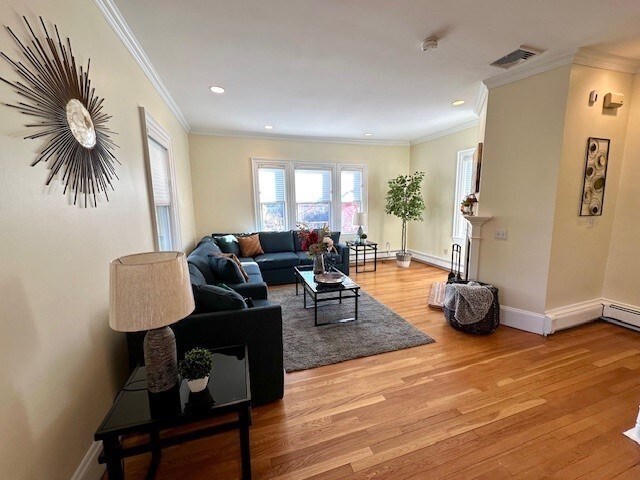 living area with crown molding, baseboards, visible vents, and light wood finished floors