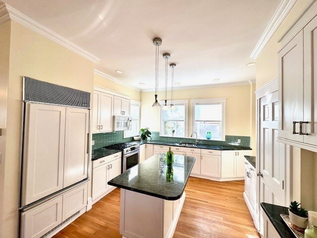 kitchen with stainless steel gas range oven, ornamental molding, a sink, light wood finished floors, and white microwave