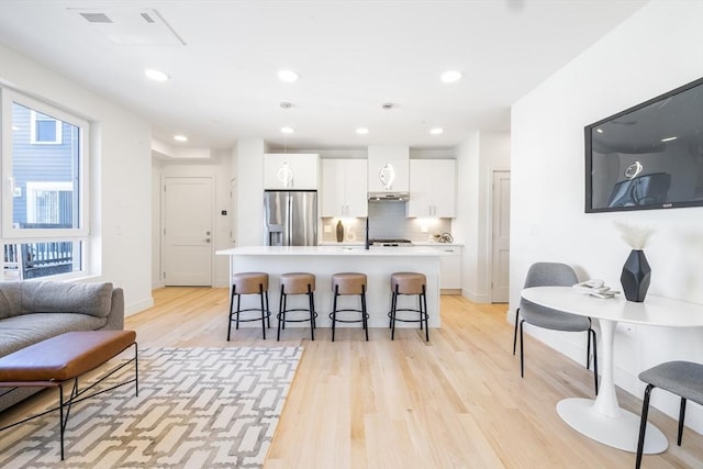 kitchen with stainless steel fridge, a breakfast bar, light hardwood / wood-style floors, white cabinetry, and an island with sink