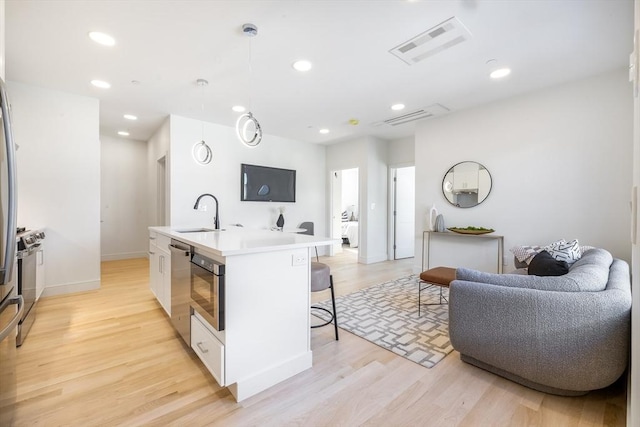 kitchen featuring sink, light hardwood / wood-style flooring, pendant lighting, a center island with sink, and white cabinets