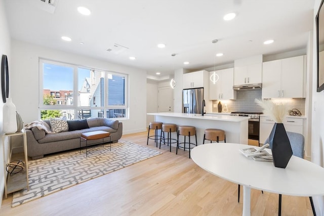 kitchen with hanging light fixtures, light hardwood / wood-style flooring, a center island with sink, white cabinets, and appliances with stainless steel finishes