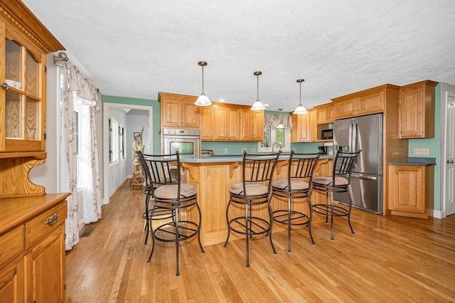 kitchen with baseboards, a breakfast bar area, stainless steel appliances, and light wood-style flooring
