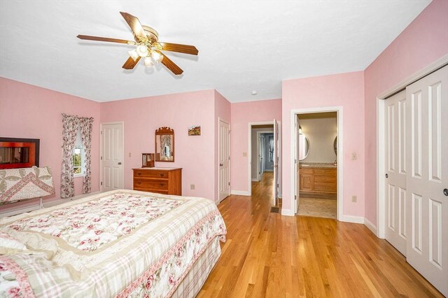 bedroom featuring two closets, baseboards, ensuite bathroom, ceiling fan, and light wood finished floors