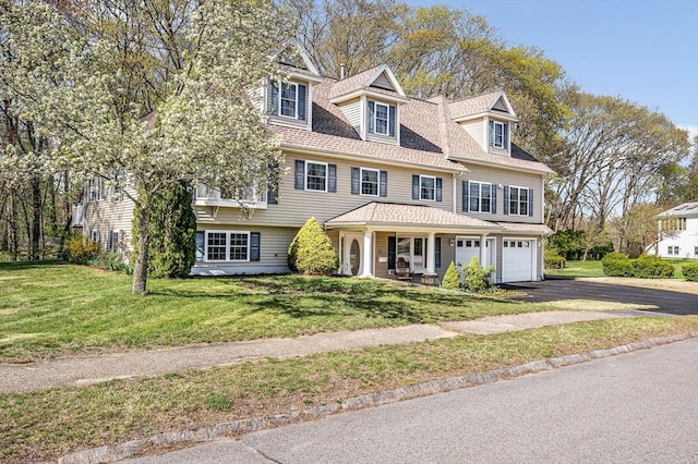 shingle-style home featuring an attached garage, a front lawn, aphalt driveway, and a porch
