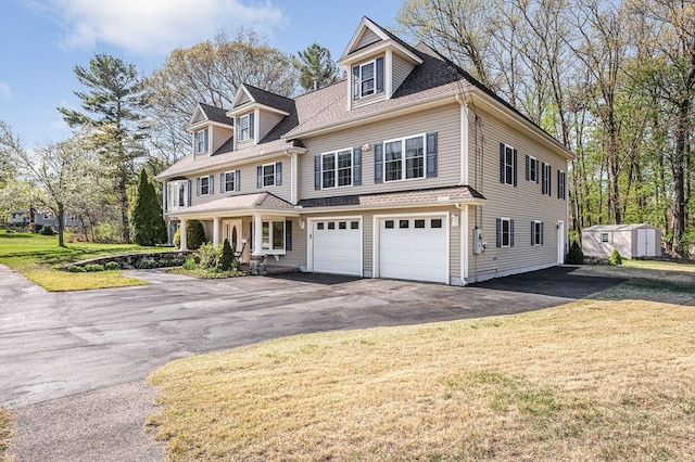 shingle-style home with an outdoor structure, a front lawn, a shed, an attached garage, and driveway
