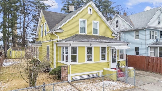 view of front of house featuring entry steps, an outbuilding, roof with shingles, fence private yard, and a shed