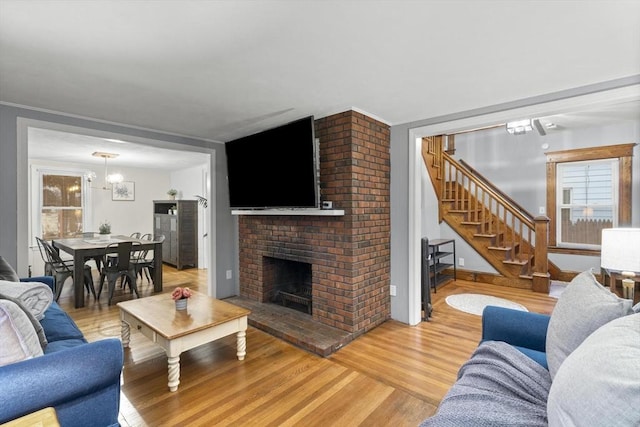 living area with a chandelier, stairway, light wood-type flooring, and a brick fireplace