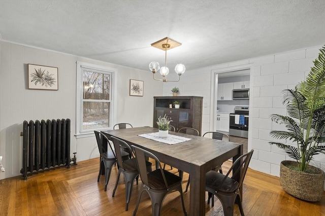 dining room with radiator, a notable chandelier, wood-type flooring, and a textured ceiling