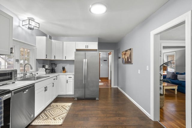 kitchen with white cabinets, dark wood finished floors, stainless steel appliances, light countertops, and a sink