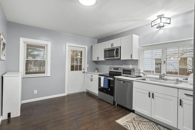 kitchen featuring white cabinets, dark wood finished floors, appliances with stainless steel finishes, light countertops, and a sink