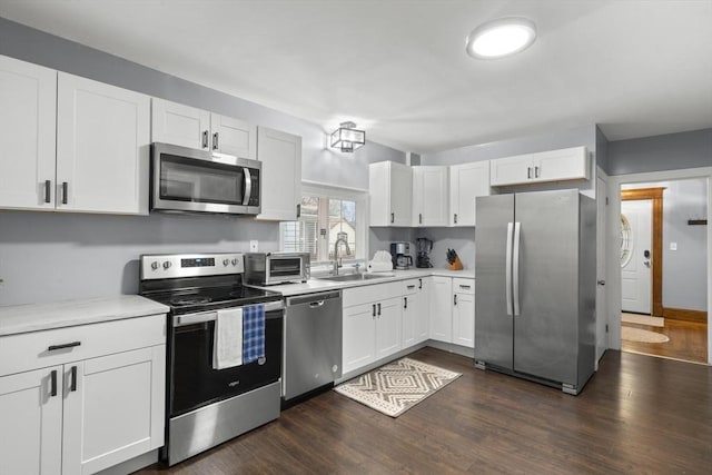 kitchen featuring white cabinets, dark wood finished floors, appliances with stainless steel finishes, light countertops, and a sink