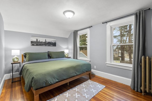 bedroom with vaulted ceiling, wood finished floors, and baseboards