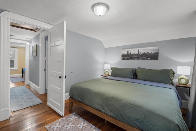 bedroom featuring attic access, vaulted ceiling, baseboards, and wood finished floors