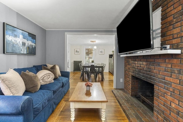 living area with ornamental molding, a brick fireplace, wood finished floors, and radiator