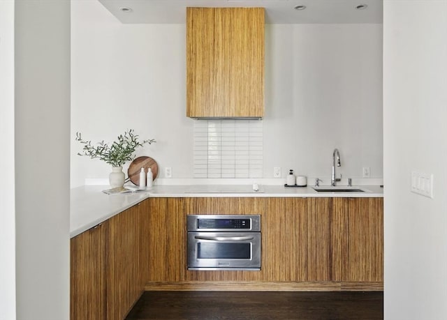 kitchen with electric cooktop, modern cabinets, light countertops, stainless steel oven, and a sink