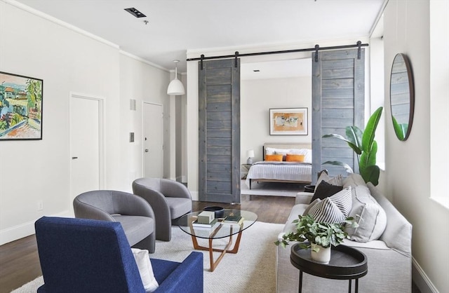 living room featuring a barn door, visible vents, ornamental molding, and wood finished floors