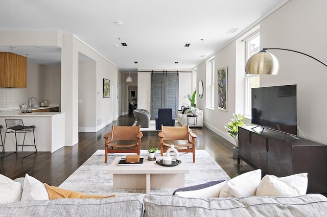 living room featuring dark wood-type flooring, baseboards, and a barn door