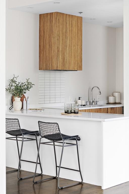 kitchen featuring wood finished floors, light countertops, brown cabinets, modern cabinets, and a kitchen bar