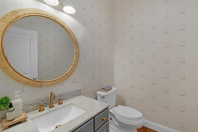half bathroom with toilet, vanity, and wallpapered walls
