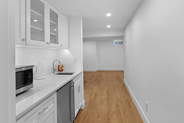 kitchen featuring a sink, appliances with stainless steel finishes, white cabinetry, glass insert cabinets, and light wood-style flooring